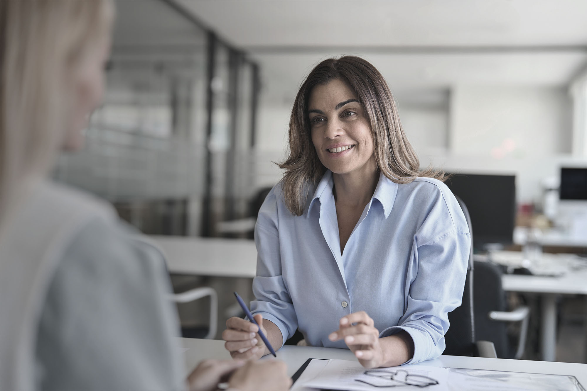 A woman smiling, holding a pen, presumably interviewing someone